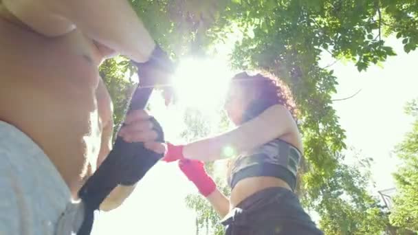 Athletic caucasian man and woman wrapping hands with bandages for workout in summer park, slow-motion — Stock Video