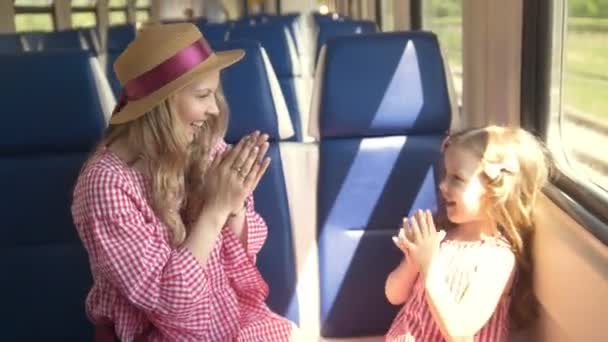 Giovane madre e figlioletta che giocano a dolcetto seduti davanti alla finestra in treno vuoto — Video Stock