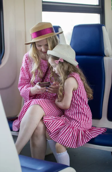 Portret van Kaukasische meisje met haar moeder in hoeden met golvend haar met behulp van een smartphone in trein — Stockfoto
