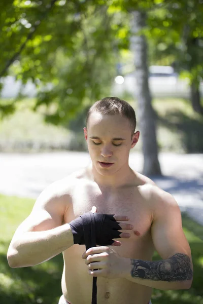 Boxer uomo atletico caucasico che avvolge le mani con bende per l'allenamento nel parco estivo — Foto Stock