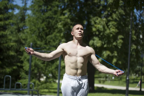 Atlético hombre musculoso saltando con una cuerda, entrenamiento al aire libre en el día soleado — Foto de Stock