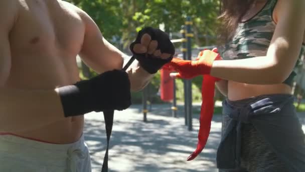 Hombre boxeador envolver sus manos joven mujer le ayuda, entrenamiento en el parque — Vídeo de stock