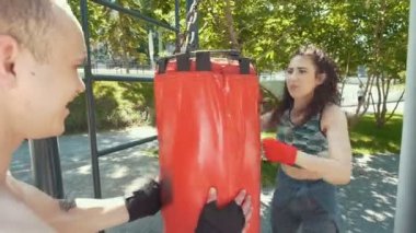 Genç adam atletik kadın güneşli gün parkta boks yapan için kum torbası tutar, yakın çekim