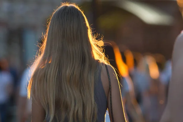 Visão traseira da jovem mulher caucasiana andando na multidão na rua pedonal no pôr do sol de verão — Fotografia de Stock