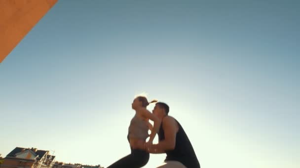 Молодая пара практикует акробатику, выполняя трюки на открытом воздухе на закате — стоковое видео