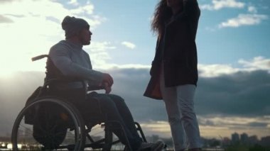 Engelli adam açık havada günbatımında konuşurken tekerlekli sandalyede olan kadın