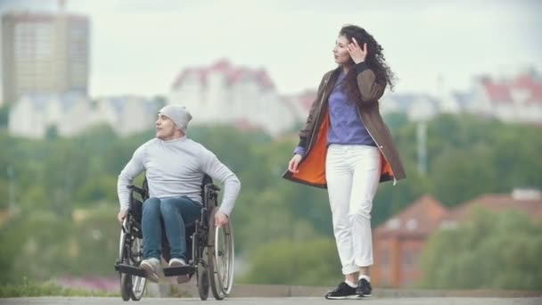 Hombre discapacitado en una silla de ruedas caminando juntos a su novia en el muelle — Vídeos de Stock