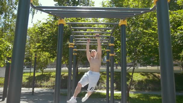 Sportlicher junger Mann trainiert an Sommertag am Reck im Park — Stockvideo