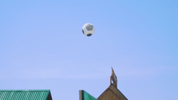 Globo de fútbol sobre un fondo de cielo azul vuela sobre los tejados — Vídeos de Stock