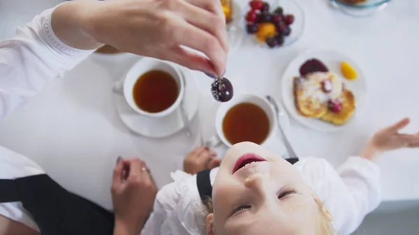 Вид сверху мамы и ее маленькой девочки пьет чай и ест вишню — стоковое фото