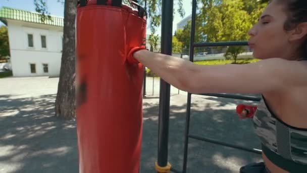 Αθλητική νεαρή γυναίκα σε αθλητικά ενδύματα χτυπάει ένα σάκο ζουμπάρισμα, προπόνηση στο πάρκο καλοκαίρι, αργή κίνηση — Αρχείο Βίντεο