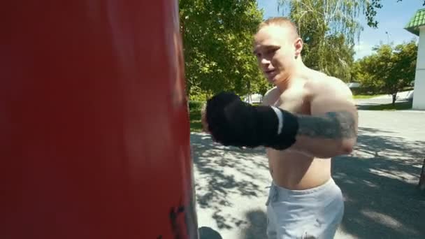 Atletisk ung man bedriver boxning med slagsäck i sommaren park — Stockvideo