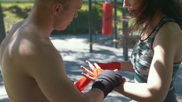 Manos de hombre y mujer jóvenes que envuelven las manos con vendas para el entrenamiento en el día de verano — Vídeo de stock
