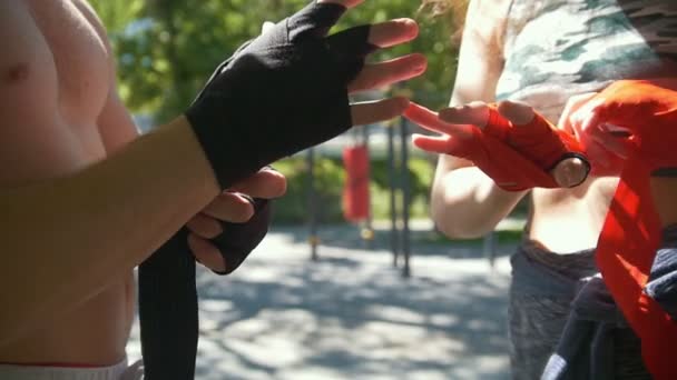 Mannelijke bokser wrap zijn handen jonge vrouw helpt hem, sporten in het park - slowmotion — Stockvideo