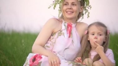 Yaz çayır üzerinde oturan baş sarılma küçük kızı üzerinde çelenk ile güzel annesi
