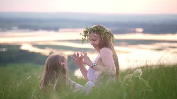 Happy mother and daughter having a rest in nature on the hill at summer sunset — Stock Video