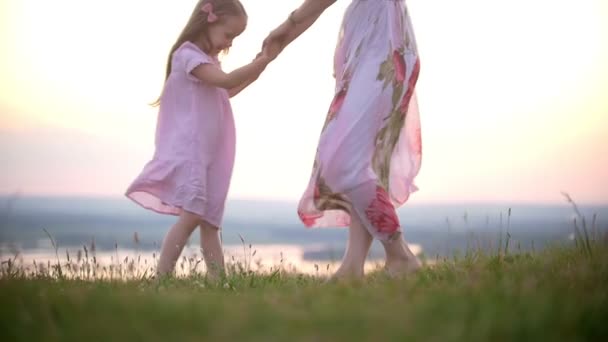 Roztomilá holčička drží za ruce s mámou dupnutí na kopci trávy při západu slunce — Stock video