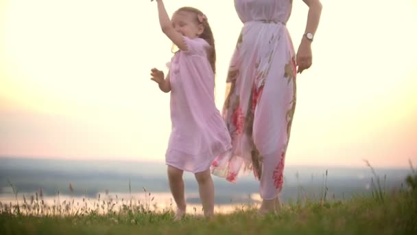 Allegro bambina che si tiene per mano la mamma che balla sull'erba collina al tramonto estivo — Video Stock