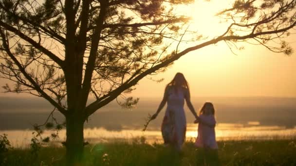 Ung glad mamma med lilla dotter gå över kullen i ljusa solnedgången — Stockvideo