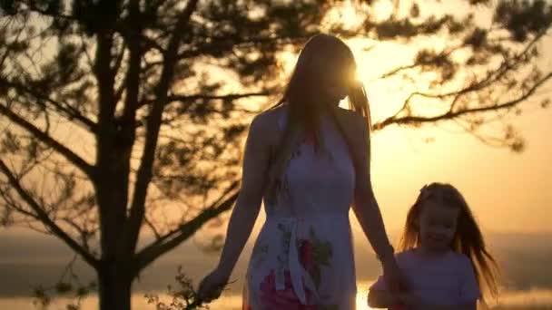 Ευτυχισμένη μητέρα και κόρη περπατώντας στον λόφο κάτω από το δέντρο στο φωτεινό ηλιοβασίλεμα — Αρχείο Βίντεο