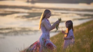 Genç Anne Anne yaz çayır on gün batımında hugs kızının kafasına çelenk koyar