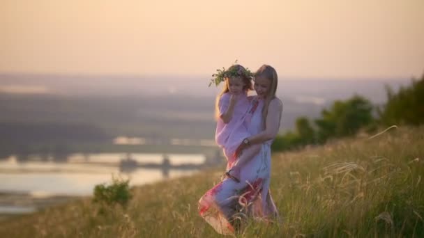 Молода мати тримає дочку в руках йде по пагорбу на літній захід сонця — стокове відео