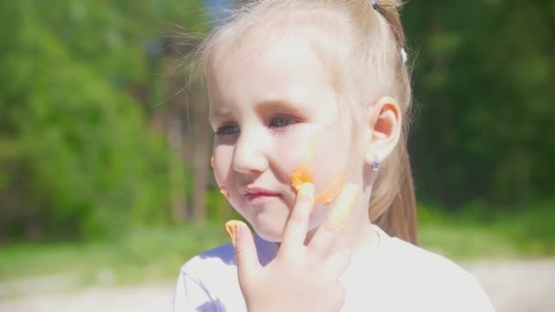 Lilla kaukasiska flicka Ritar linjer på läpparna med finger färger på sommardag utomhus — Stockvideo