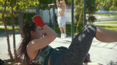 Genç kadın fitness egzersizleri çekti çubuğu'nda açık havada güneşli gün kadar kaslı adam önünde yapıyor