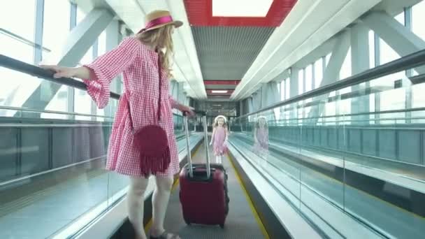 Młoda atrakcyjna kobieta z walizką, idąc w dół schodów ruchomych i jej urodziwa córka biegnie po matce na lotnisku — Wideo stockowe