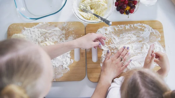 Mom and daughter hands sprinkles flour on the board for preparing pancakes