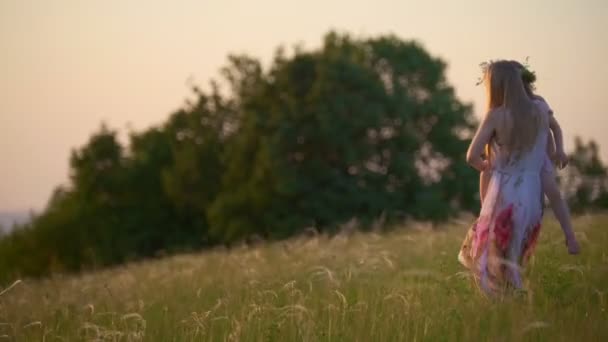 Молодая мать, держащая дочь на руках, спускается с холма на летнем закате — стоковое видео