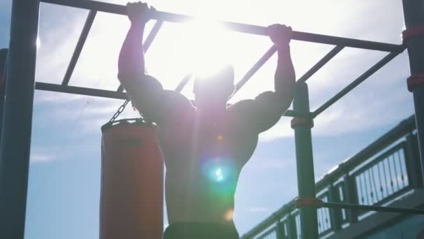 Rear view of muscular man pulled-up on horizontal bar outdoors at sunny day — Stock Video