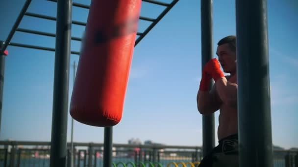 Atletische man bezig in boksen met bokszak in de zomer buiten, slow-motion — Stockvideo