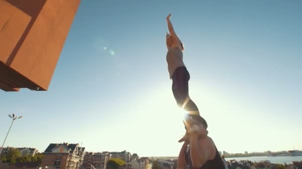Молода акробатична пара, виконуючи фліп, молодий чоловік кидає жінку в повітря, балансуючи на руках під час заходу сонця на відкритому повітрі — стокове відео