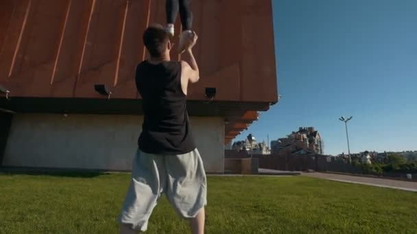 Joven pareja acrobática realizando voltereta, joven hombre lanza una mujer en el aire equilibrio en sus brazos al atardecer al aire libre — Vídeos de Stock