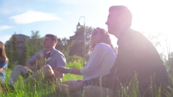 Friends looks at the clouds sitting on the grass under the sun — Stock Video