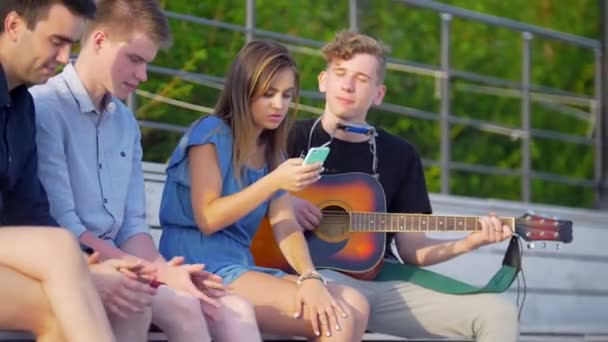 Jonge vrienden hipsters hebben een rust in het park en luisteren naar liedjes met gitaar — Stockvideo