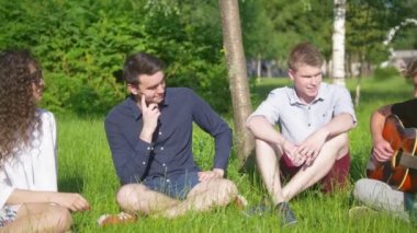 Genç mutlu arkadaş grubunuz bir dinlenme çimenlerin üzerinde genç adam gitar çalmak
