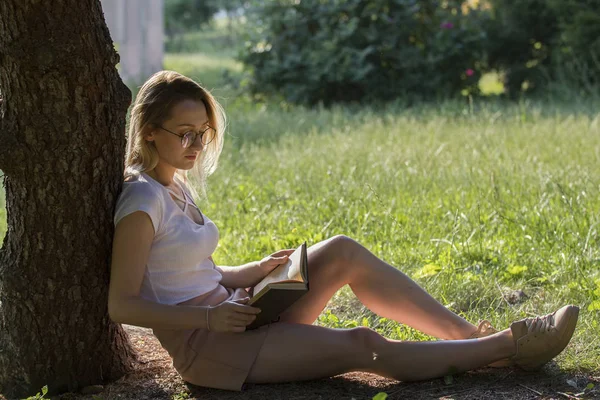 晴れた日に 水平で公園の木の下で本を読んで若い魅力的な女性 — ストック写真
