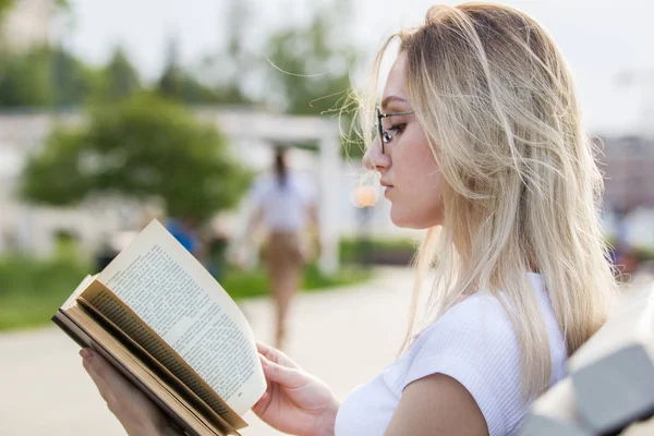 Retrato de mulher atraente lendo um livro sentado no banco no dia de verão — Fotografia de Stock