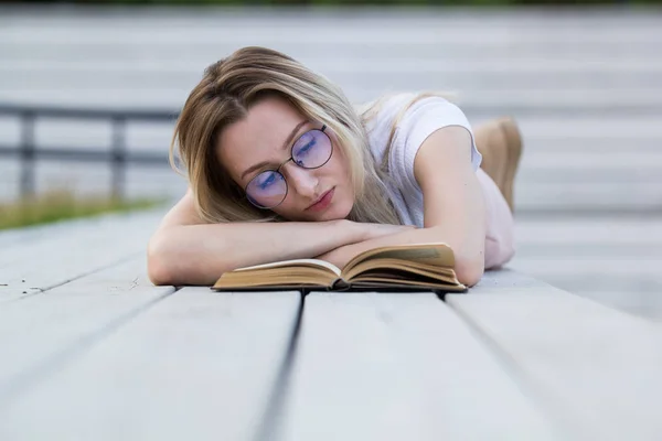 Schöne junge Frau liest ein Buch, das auf der Bank im Park liegt — Stockfoto