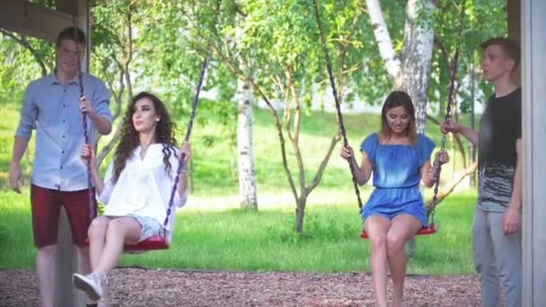 Deux jeunes hommes se balancent sur le swing de leurs belles filles dans le parc d'été — Video