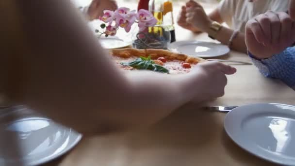 Hands of waiter sets on the table a pizza to the young friends in restaurant — Stock Video