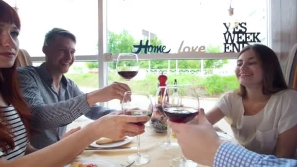 Young happy friends clink glasses of red wine and drinking in restaurant — Stock Video