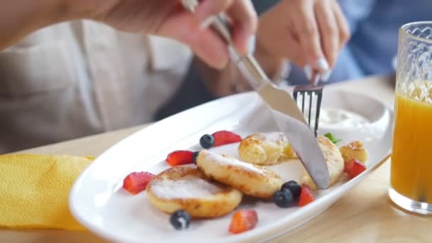 Vrouwelijke handen snijdt een smakelijke kwark pannenkoeken met een mes en vork in restaurant — Stockvideo