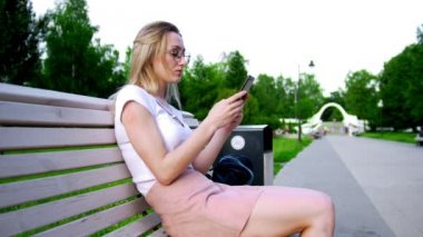 Genç çekici kadın smartphone bir ileti yazıyor ve bankta oturan eski bir kitap alır