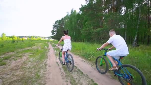 Young couple cycling through the spruce branches in summer forest — Stock Video