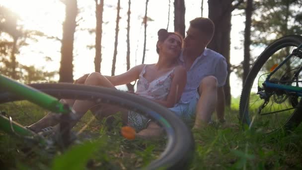Jeune couple caucasien se reposer sur l'herbe après avoir fait du vélo dans la forêt — Video