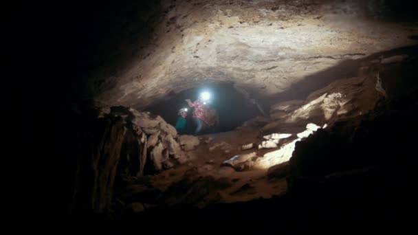 Crianças em capacetes com lanternas entram em uma caverna escura — Vídeo de Stock