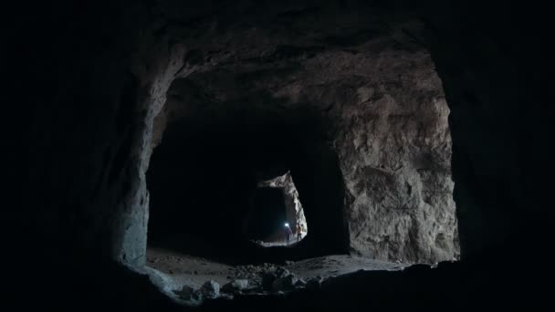Група підлітків заходить у темну печеру з ліхтариками — стокове відео